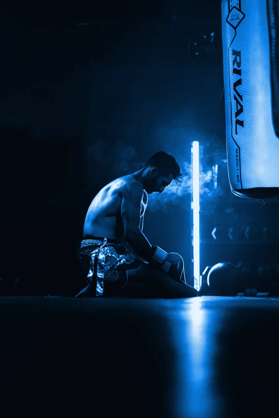 Boxeador descansando junto a la bolsa bajo una luz azul